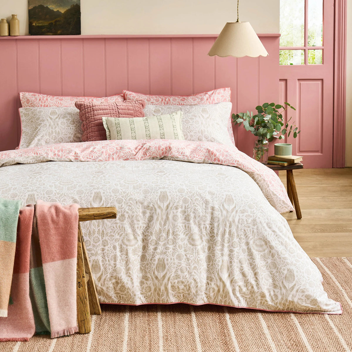 Floral patterned bedding set with pink pillows and a pink paneled wall in a bedroom.