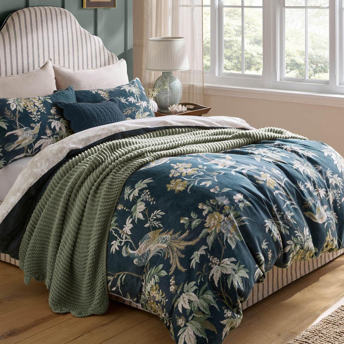 Floral pattern bedding set with blue duvet, green throw, and striped headboard in a bedroom.