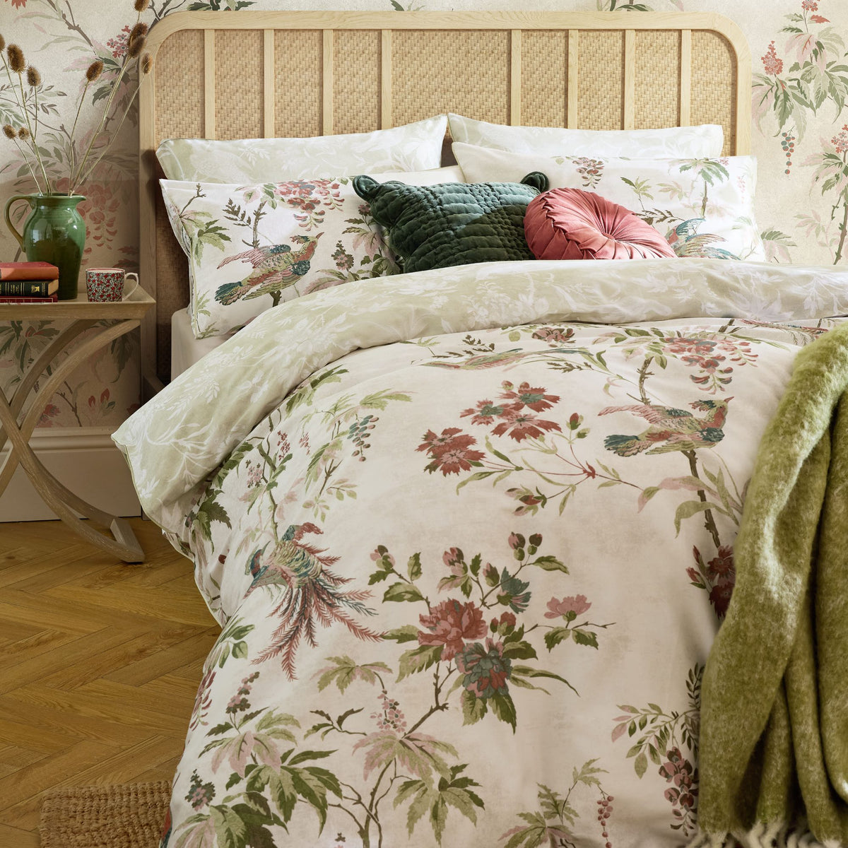 Floral bird print duvet cover set with green and pink decorative cushions on a cane headboard bed.