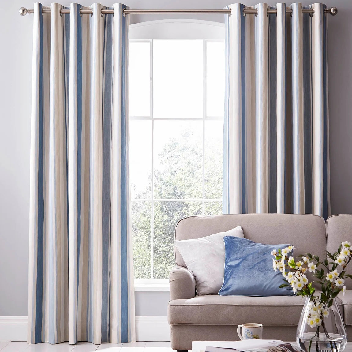 Blue and beige striped curtains hanging on a silver rod next to a grey sofa with cushions.