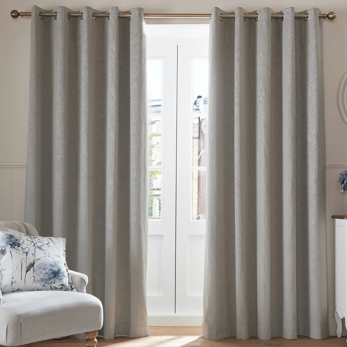 Light grey patterned eyelet curtains hanging on a gold rod by a white French door.
