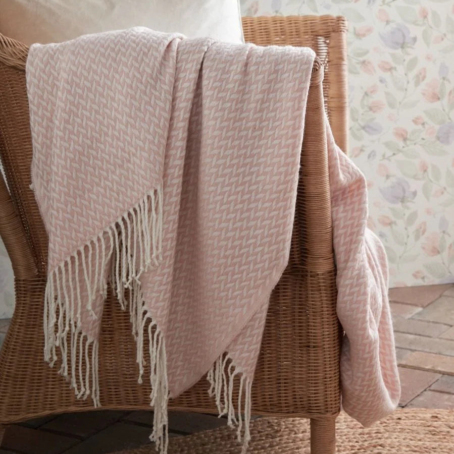 Pink textured herringbone pattern throw blanket with fringe draped over a wicker chair
