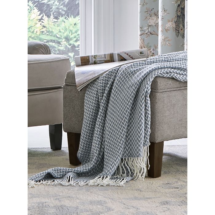 Grey and white herringbone pattern throw blanket draped over a grey upholstered ottoman