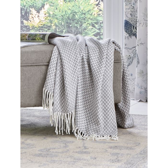 Grey and white chevron patterned throw blanket with tassels on a beige ottoman